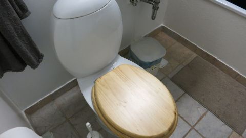 Ein Toilettenspülkasten ist sichtbar, läuft langsam voll und steht in einem Badezimmer mit einem Holzdeckel.
