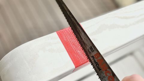 Ein Holzstück wird mit einer Stichsäge geschnitten, während es auf einem Holztisch im Freien liegt.