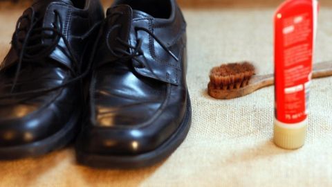 Ein Paar schwarze Schuhe liegt neben einer weichen, ausgetrockneten Schuhcreme und einer Bürste auf einem Tisch.