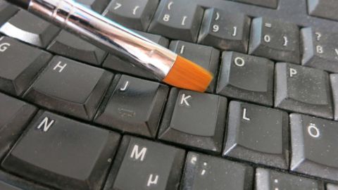 Eine PC-Tastatur wird mit einem Pinsel gereinigt, um Schmutz von den Tasten zu entfernen und die Hygiene zu verbessern.