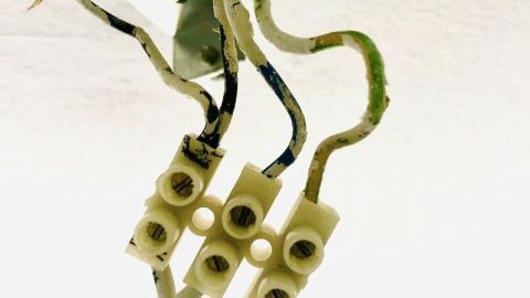 Eine Lüsterklemme verbindet farbige Kabel, während eine Lampe in einem Zimmer installiert wird.