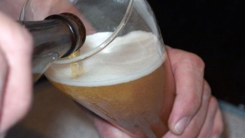 Ein Glas Weizenbier wird gerade aus einer Flasche eingeschenkt, der Schaum bildet sich an der Oberkante.