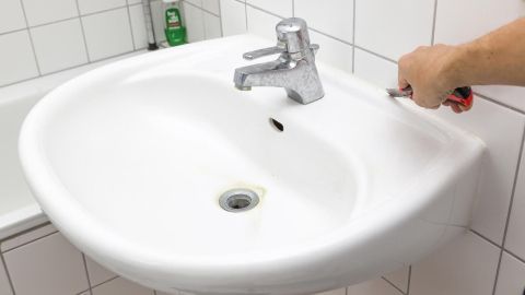 Ein Badezimmerwaschbecken wird gereinigt, während die Hand einen Schwamm hält. Schimmel im Bad ist sichtbar.