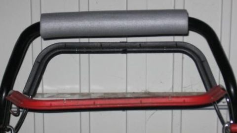 Der Griff eines Rasenmähers ist mit Schaumstoff ummantelt, um Vibrationen und Erschütterungen zu dämpfen, vor einer weißen Wand.