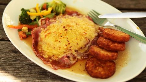 Ein Putenschnitzel mit Käse überbacken liegt auf einem Teller, umgeben von Gemüse und Rösti.