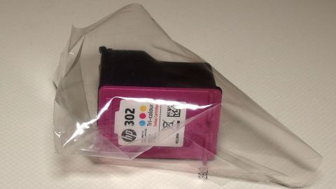 Eine Druckerpatrone in einer transparenten Verpackung liegt geschützt auf einer glatten Oberfläche, bereit zur Verwendung.