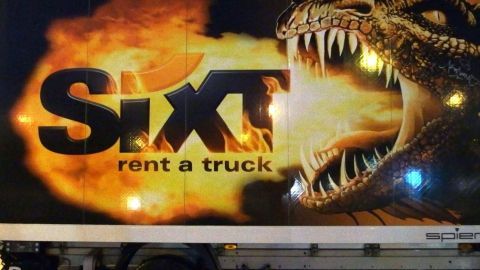 Ein Transporter mit einem auffälligen Werbemotiv zeigt einen Drachen und den Schriftzug „Sixt rent a truck“ im Hintergrund.
