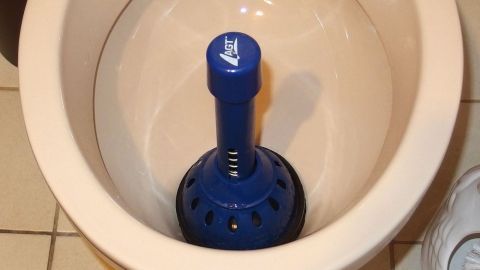 Ein blauer Pömpel steht in einer verstopften Toilette, bereit, das Problem im Badezimmer zu lösen.