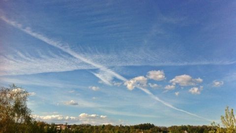 Ein klarer Himmel mit weißen Wolken und einem langen Kondensstreifen zeigt die Himmelsrichtung ohne Kompass.