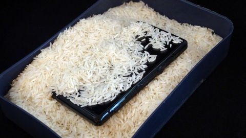 Ein schwarzes Handy liegt auf einem Bett aus Reis, um es nach einem Wasserschaden zu trocknen.