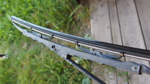 Ein Scheibenwischer mit Gummiblatt, das in einem grünen Umfeld auf einem Holzdeck steht, wird sichtbar gepflegt.