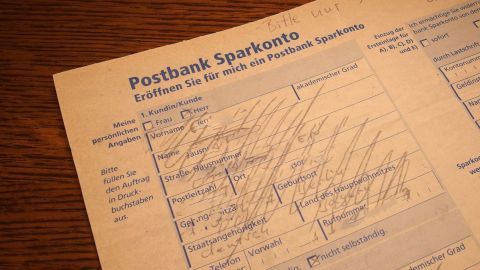 Um im Urlaub Gebühren für Geldabhebungen zu sparen, solltest du ein kostenfreies Konto bei einer Bank nutzen, die keine internationalen Abhebungsgebühren erhebt. Informiere dich über die besten Optionen, bevor du verreist. Ein ausgefülltes Formular mit handschriftlichen Angaben liegt auf einem Tisch, um Gebühren für Geldabhebungen zu sparen.