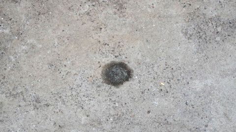 Ölflecken auf dem Garagenboden entfernen mit Katzenstreu oder Sand. Der Garagenboden zeigt eine verschmutzte Stelle, während der gesamte Bodenbereich Beton bleibt.