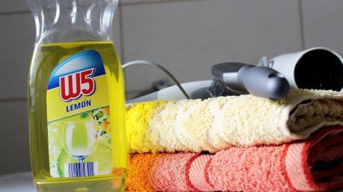 Flasche Spülmittel steht neben bunten Handtüchern auf einer Ablage in einem Badezimmer, bereit zum Haare waschen.