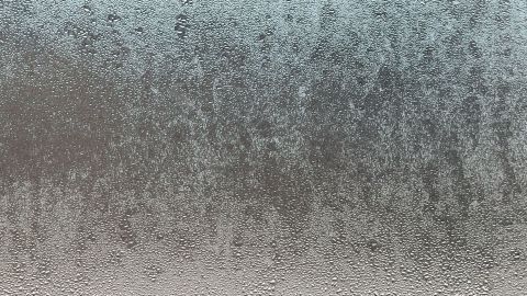 Eine beschlagene Autoscheibe zeigt Wassertröpfchen auf der Oberfläche, während winterliche Bedingungen im Hintergrund erkennbar sind.
