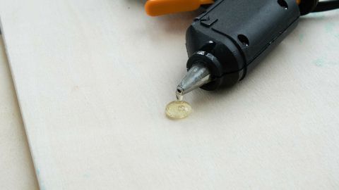 Ein Heißkleber wird aus einer Klebepistole auf eine Holzplatte aufgetragen, um Kabel zu verlegen und zu fixieren.
