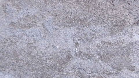 Der lose Putz hat sich an der Wand gelöst, während der graue Untergrund uneben und strukturiert aussieht.