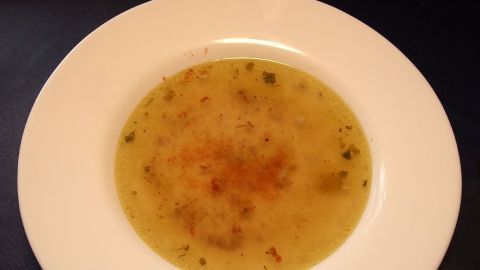 Eine klare Suppe in einer weißen Schüssel, die leicht gewürzt ist und auf einem dunklen Tisch steht.