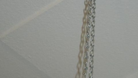 Eine Duschvorhangstange hängt mit einer Kette an der Decke über einer Badewanne und sichert den Duschvorhang.