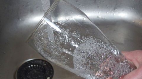 Ein Glas wird unter fließendem Wasser gereinigt, um Schaum für das Bier zu entfernen, während es in einem Spülbecken steht.