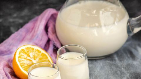 Wer gerne Cocktails trinkt, sollte auch mal den Eskimo, ein Cocktail aus Wodka und Milch ausprobieren. Ein klarer Krug mit einem weißen Cocktail aus Wodka und Milch steht neben zwei kleinen Gläsern auf einem lila Tuch, mit einer Zitrone im Hintergrund.