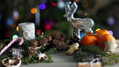 Dekorative Weihnachtsfiguren und -schmuck liegen auf einem Tisch, umgeben von Tannenzweigen und bunten Lichtern.