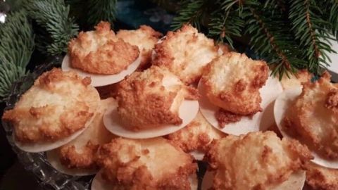 Mit Kondensmilch eingepinselte Kokosmakronen werden beim Backen schneller braun und bekommen eine schöne Farbe. Lecker gebräunte Kokosmakronen liegen auf einer Servierplatte, umgeben von grünen Tannenzweigen, ideal für festliche Anlässe.