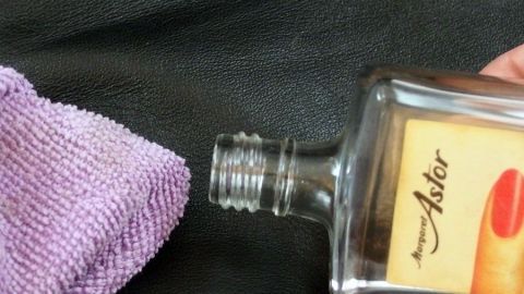 Kratzer in der Leder-Aktentasche mit Nagellackentferner (Aceton) glattpolieren. Eine Leder-Aktentasche wird mit einem Reinigungstuch und einer Flasche zum Entfernen von Kratzern behandelt.