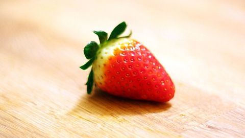 Eine saftige Erdbeere liegt auf einem hellen Holzuntergrund, ideal für weiche Haut und gesunde Ernährung.