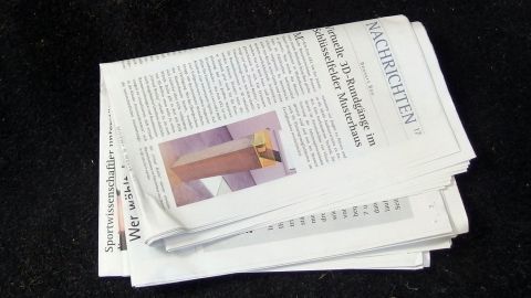 Eine Zeitung liegt auf einem schwarzen Untergrund, bereit gelesen zu werden, während im Auto auf Nachrichten gewartet wird.