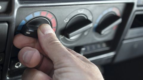 Ein Hand drückt den Heizungsregler im Auto, während es in einem Fahrzeugkontext kühl ist und die Heizung nicht funktioniert.