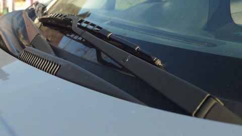 Schmierende Scheibenwischer: Einfach einen in Essig getränkten weichen Lappen mehrmals über die Wischblätter ziehen. Ein Scheibenwischer ist auf einer Fahrzeugfront montiert und bereit, bei Regen die Sicht zu verbessern.