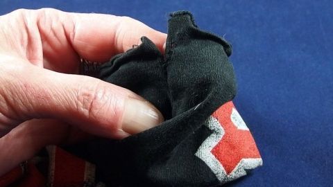 Eine Hand hält einen Stoffrest mit eingerissener Naht, bereit zur Blitzreparatur von Kleidung auf einem blauen Hintergrund.