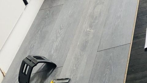 Laminatplanken liegen auf dem Boden, während Werkzeug zur Verlegung in einer hellen Raumumgebung bereitliegt.