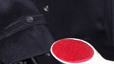 Eine Fusselbürste mit roter Borstenseite reinigt effektiv die Kleidung neben einem schwarzen Hemd mit Knöpfen.