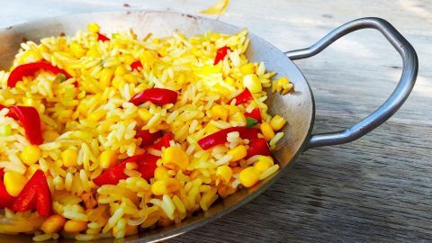 Eine bunte Gemüsepfanne mit gelbem Reis, Paprika und Mais steht auf einem Holzuntergrund, bereit zum Servieren.