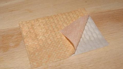 Ein Stück orange Tapete wird auf einer Holzoberfläche leicht angehoben, um den weiß gemusterten Rückseitenbereich zu zeigen.