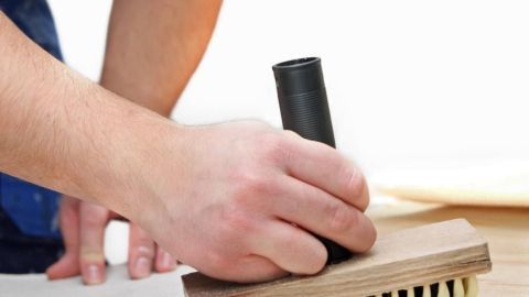 Eine Hand drückt einen Tapetenroller auf eine Holzplatte, während jemand Tapetenkleister vorbereitet.