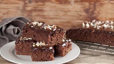 Auf einem weißen Teller liegen braune Lebkuchenstücke mit Schokoladenglasur, umgeben von Holz und einemTuch.
