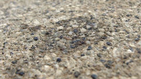 Ein Ölfleck auf einer rauen, grauen Betonoberfläche ist sichtbar, der durch das Spülmittel entfernt werden soll.