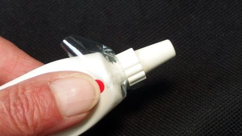 Eine Hand hält eine Tubenpaste mit einem sauberen, nicht eingetrockneten Ausguss, bereit zum Kneten in einem dunklen Umfeld.