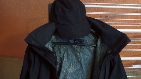 Eine schwarze Regenjacke hängt neben einer passenden Mütze an einem Haken, bereit für einen Einsatz im Regen.