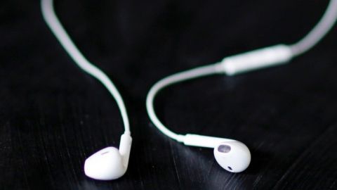 Weisse Kopfhörer liegen auf einem schwarzen Tisch, bereit zur Reinigung mit Klebeband, um Schmutz zu entfernen.
