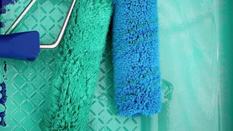 Farbrollen liegen in einer Farbwanne. Eine Rolle ist blau, die andere grün, und die Wanne hat eine geriffelte Fläche.