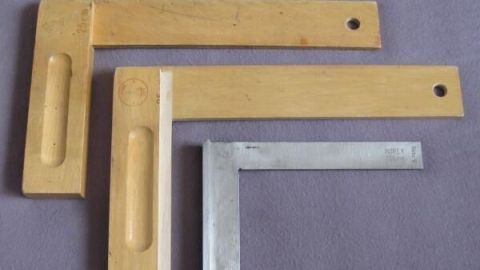 Zwei Schlosserwinkel liegen auf grauem Stoff. Der größere ist aus Holz, der kleinere aus Metall mit Gravur "RIEFLY DIN 875/0".