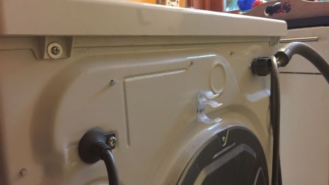 Eine Waschmaschine zeigt die Rückseite mit Wasseranschlüssen und einem offenen Zugang, ideal für den Austausch der Türdichtung.