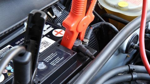 Zwei Klemmen sind an einer Autobatterie befestigt, während eine Überbrückung durchgeführt wird, um den Motor zu starten.