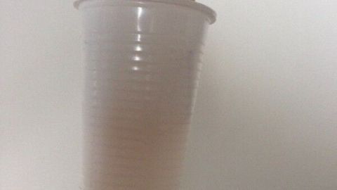 Ein Pinsel mit einem Plastikbecher an der Spitze steht, um beim Streichen das Kleckern zu verhindern.