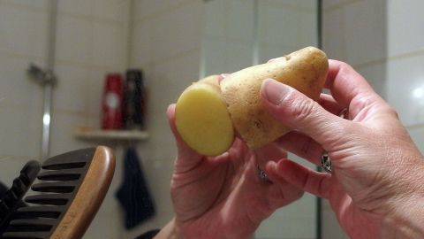 Blitzende Spiegel: Spiegel mit Kartoffel abreiben und dann trockenreiben. Ein Mensch hält eine Kartoffel mit einem abgerundeten Ende in einer Badezimmerumgebung, während der Hintergrund unscharf bleibt.