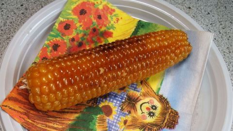 Gegrillter Mais liegt auf einem bunten Servietten mit Blumen und einer fröhlichen Figur, serviert auf einem Teller.